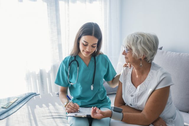 Nurse doing blood pressure monitoring for senior woman at home. Close up photo of blood pressure measurement. Nurse measuring blood pressure of senior woman at home. Smiling to each other.