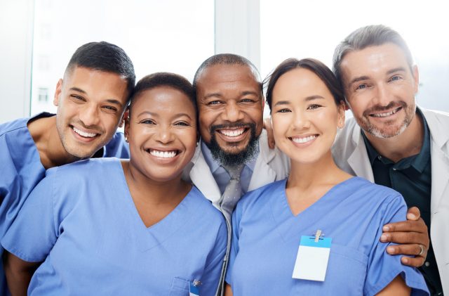 Shot of a cheerful group of doctors standing with their arms around each other inside of a hospital during the day