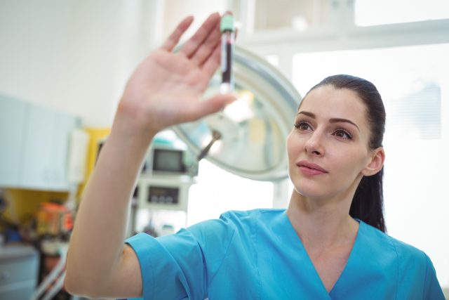 A phlebomotist looking at a vial of blood
