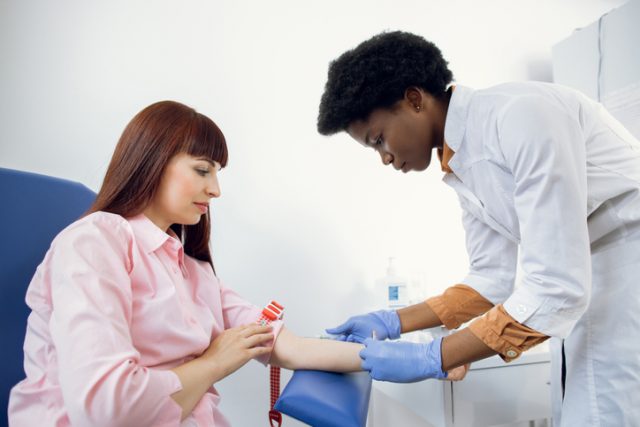 Preparation for blood test. Beautiful young African woman doctor in white medical uniform ready to take blood sample from patient's vein
