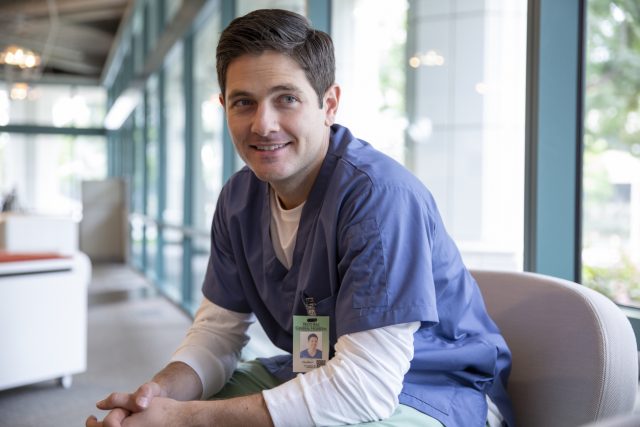 Portrait smiling male nurse in scrubs in clinic corridor