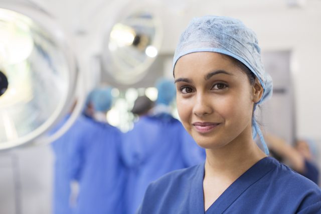 Portrait of smiling female surgical nurse wearing blue surgical cap and scrubs