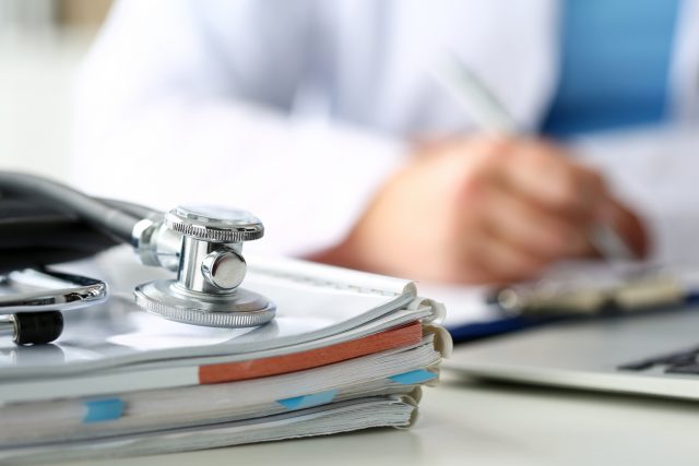 Stethoscope head lying on medical forms closeup