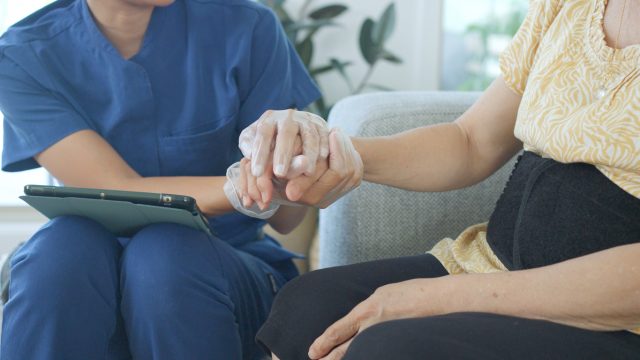 home caregiver holding hands and consoling Asian senior woman during a home visit