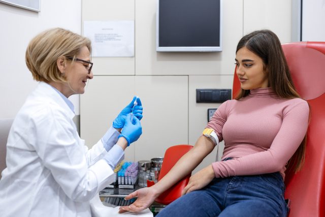 Preparation for blood test by female doctor medical uniform on the table in white bright room. Nurse pierces the patient's arm vein with needle blank tube.