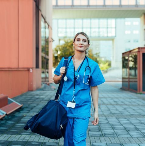 A young female LPN is walking with a gym bag and wearing scrubs